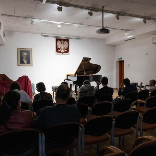 scena auli w państwowej szkole muzycznej w głubczycach, na scenie otwarty fortepian i zestaw perkusyjny zasłonięty czerwoną płachtą, na pierwszym planie osoby siedzące na publiczności