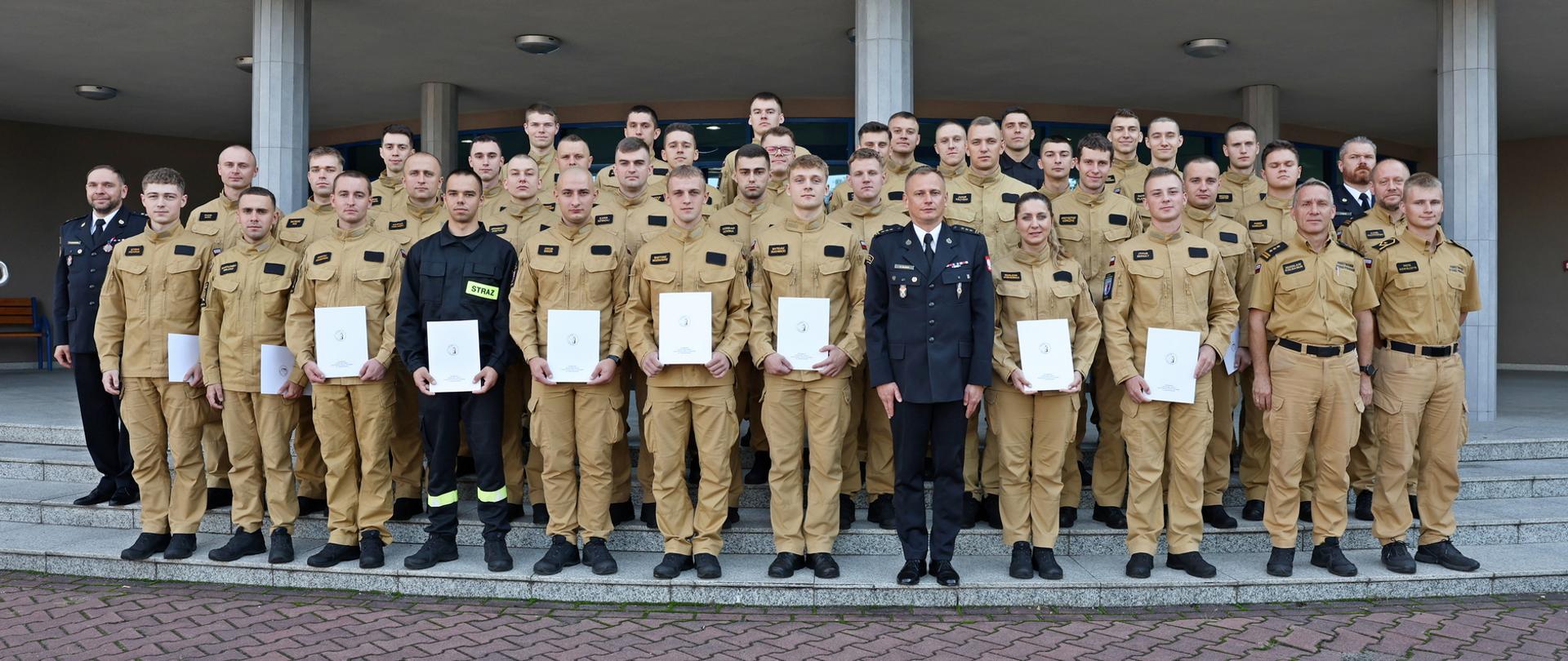 Pamiątkowe zdjęcie grupowe funkcjonariuszy IV turnusu Szkolenia Podstawowego w Zawodzie Strażak (36 osób) w towarzystwie Zastępcy Komendanta CS PSP oraz pięcioma funkcjonariuszami kadry dydaktycznej CS PSP