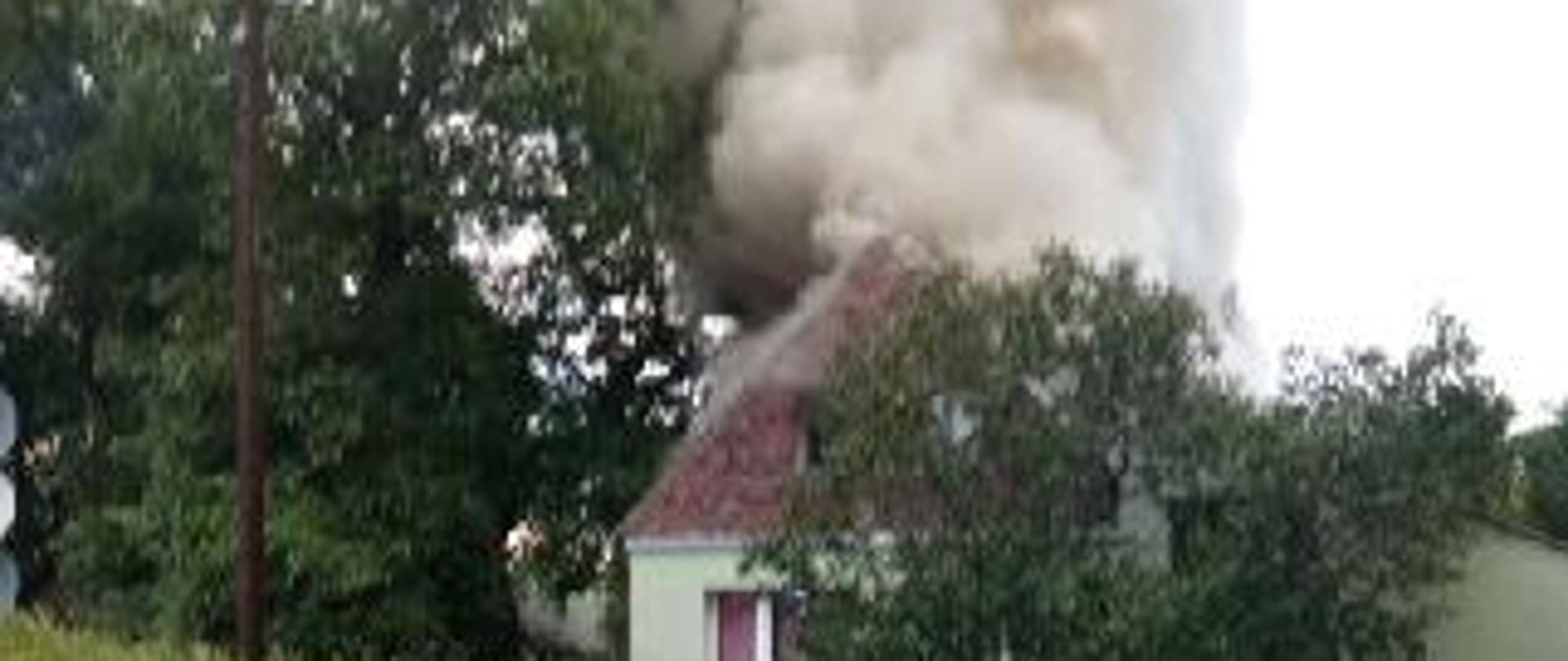 Widać ciemny dym palącego się budynku gospodarczego połączonego z mieszkalnym.