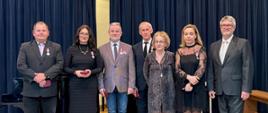 Zdjęcie wykonane jest na scenie, na tle granatowej kotary i drewnianej podłogi. W kolejności od lewej stoją :Mirosław Jaroszuk, Katarzyna Makal-Żmuda, Bogusław Rząsa, Ryszard Jasionowski, dyrektor szkoły Małgorzata Michałowska, Monika Łukawska, wizytator Centrum Edukacji Artystycznej Andrzej Bukowski. Odznaczeni nauczyciele mają pzypięte medale po swojej lewej stronie a czerwone pudełeczka trzymają w ręku.
