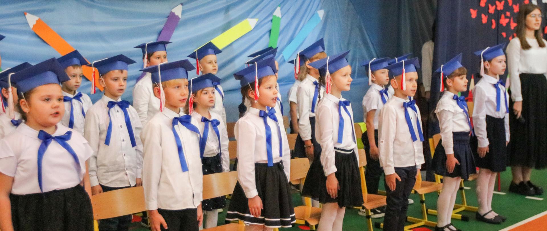 Grupa dzieci w galowych strojach stojąca na baczność.