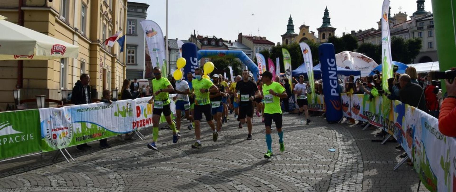 Zdjęcie zrobione na ulicy Przemyśla. Na zdjęciu biegnące osoby dopingowane z lewej i prawej strony przez widzów.
