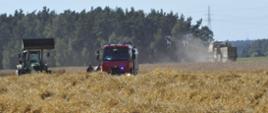 Pole ze zbożem. W tle widać samochód strażacki i traktor. Dalej widać kombajn, który kosi zboże.