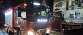 Na zdjęciu w porze nocnej widać samochód strażacki zaparkowany podczas działań usuwania skutków ulewy pod jedną z posesji w Ostrowcu Św. W tle budynek jednorodzinny.