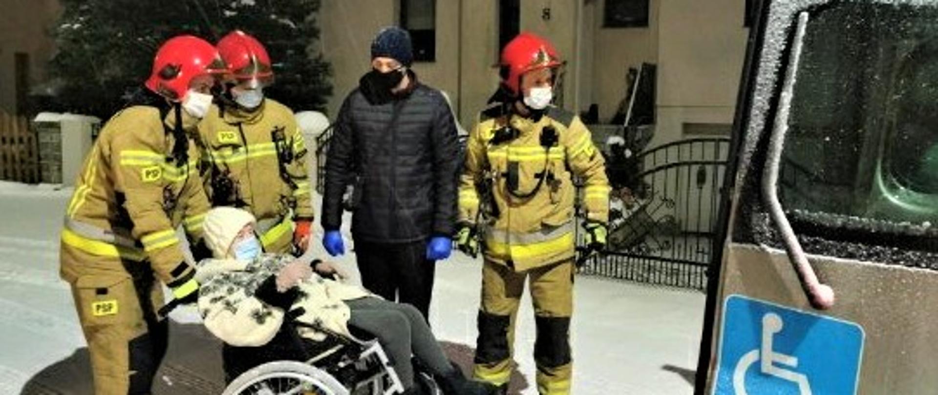 Zdjęcie przedstawia osobę na wózku, której strażacy pomagali w transporcie na szczepienie COVID-19