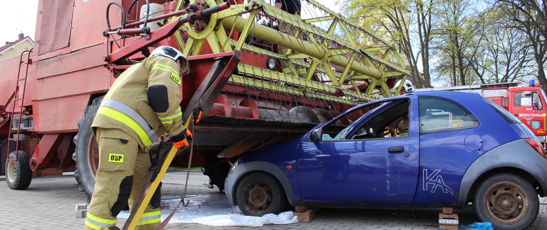 Na zdjęciu pojazd osobowy zderzył się z maszyną rolniczą - kombajnem zbożowym. Wewnątrz pojazdu osobowego osoba poszkodowana. Trwają działania ratownicze. 