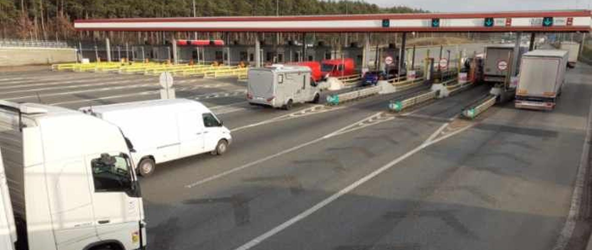 Dojazd do istniejącego punktu poboru opłat na autostradzie, tak zwane bramki. Widoczne samochody zbliżające do punktu i przejeżdżające przez punkt. 