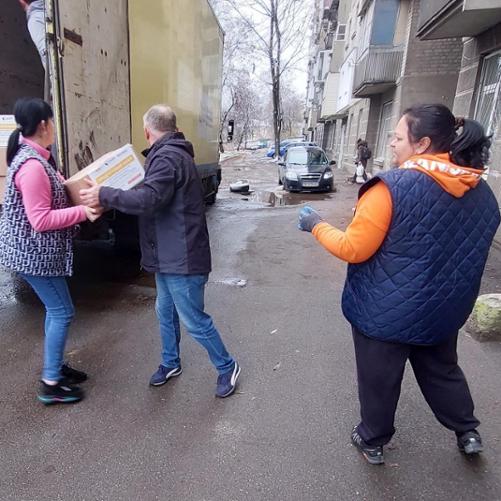Kobieta i mężczyzna wyciągają paczki z ciężarówki zaparkowanej na ulicy i podają je kolejnej kobiecie.