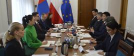 Na sali po obu stronach podłużnego stołu siedzi dziesięć osób, rozmawiają, za stołem pod ścianą flagi Polski, Mongolii i UE.
