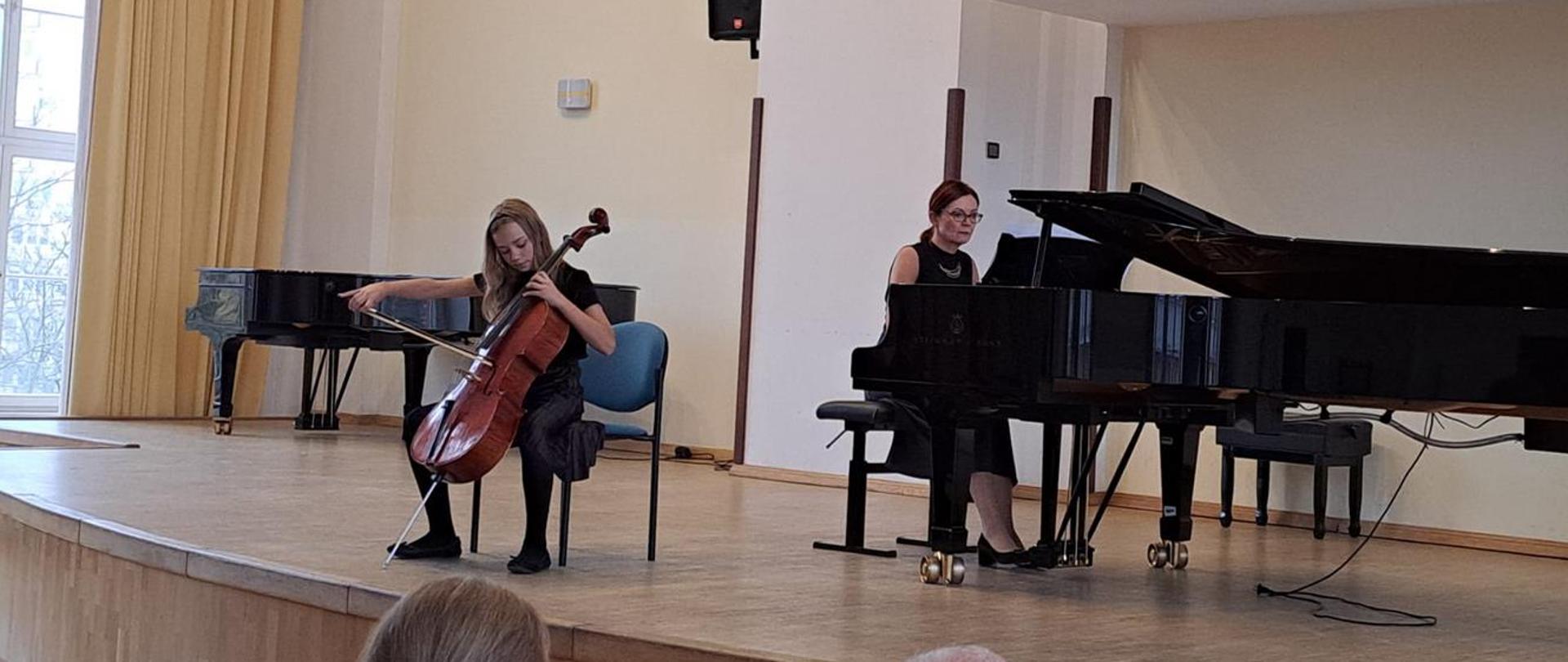 Zdjęcie kolorowe. Dziewczynka na estradzie w Akademii Muzycznej w Gdańsku wykonuje utwór muzyczny. Przy fortepianie siedzi pani akompaniatorka.