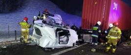 Zniszczona biała kabina pojazdu ciężarowego, leżąca przy ramie ciągnika siodłowego. Całość jest mocno odkształcona. Przy kabinie pracuje 6 strażaków w ubraniach specjalnych. W tle po lewej śnieg leżący na poboczu, po prawej czerwony, stalowy kontener.
Paweł Zdun
