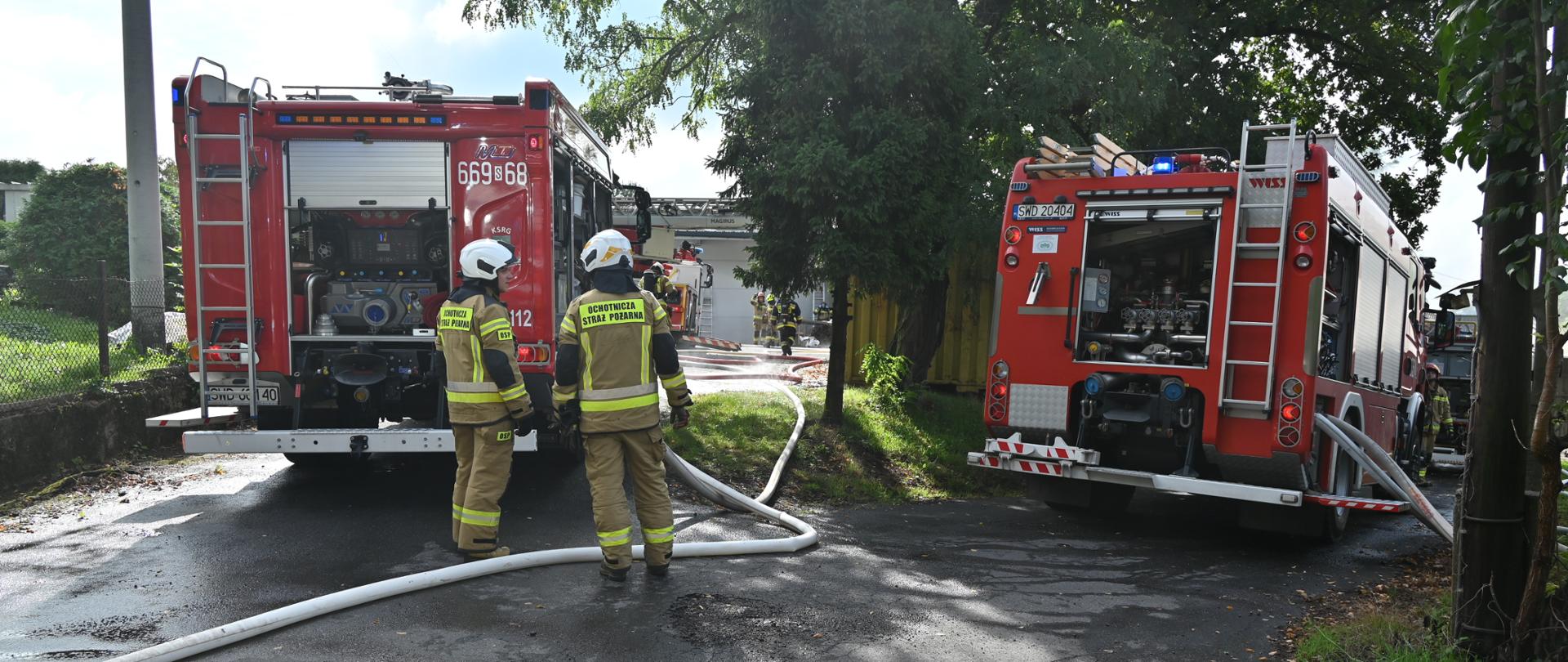 Strażacy obsługują autopompy na samochodach pożarniczych podczas pożaru