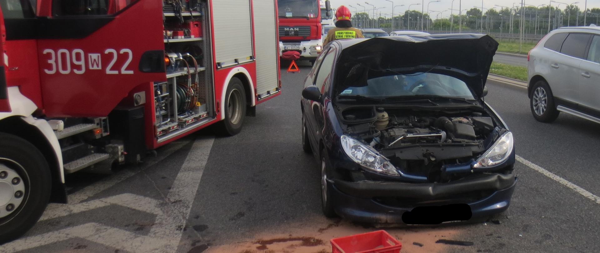 Na zdjęciu widoczny jest uszkodzony samochód osobowy, ma podniesioną maskę, obok stoii samochód straży pożarnej.