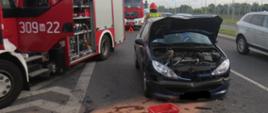 Na zdjęciu widoczny jest uszkodzony samochód osobowy, ma podniesioną maskę, obok stoii samochód straży pożarnej.