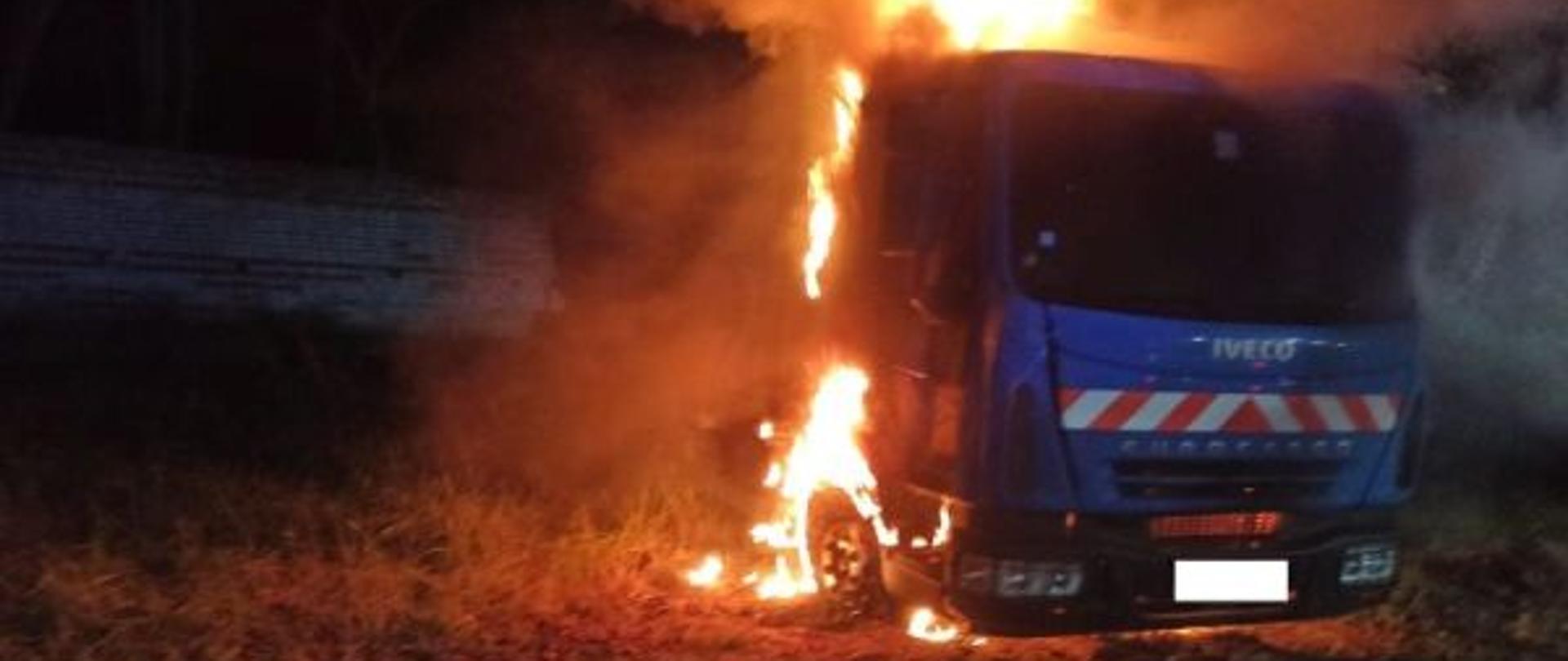 Zdjęcie wykonane w nocy. Centralny punkt zdjęcia stanowi kabina auta ciężarowego. Kabina objęta ogniem. Zdjęcie rozświetla palące się auto.