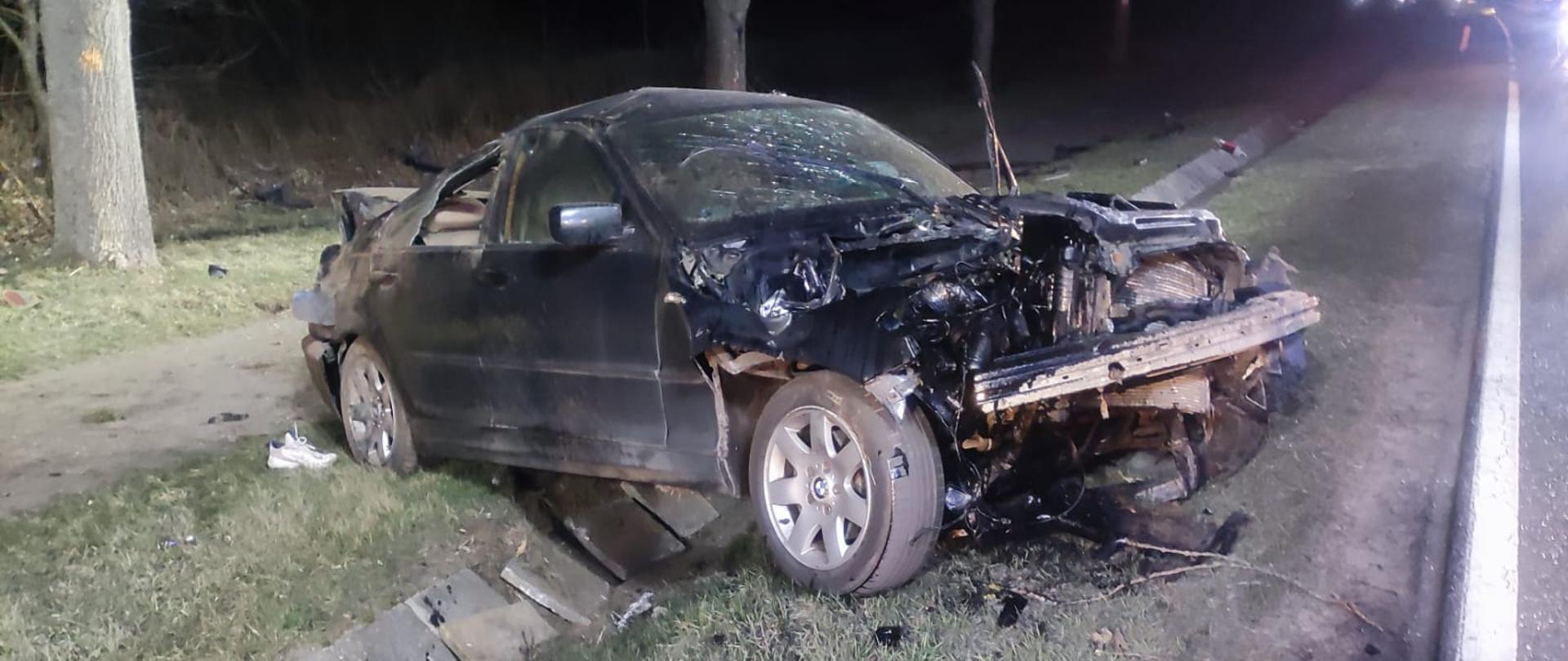 Zdjęcie przedstawia zniszczony samochód osobowy znajdujący się w pasie drogi krajowej nr 29, który brał udział w zdarzeniu. Zdjęcie wykonane zostało w porze wieczornej. 
