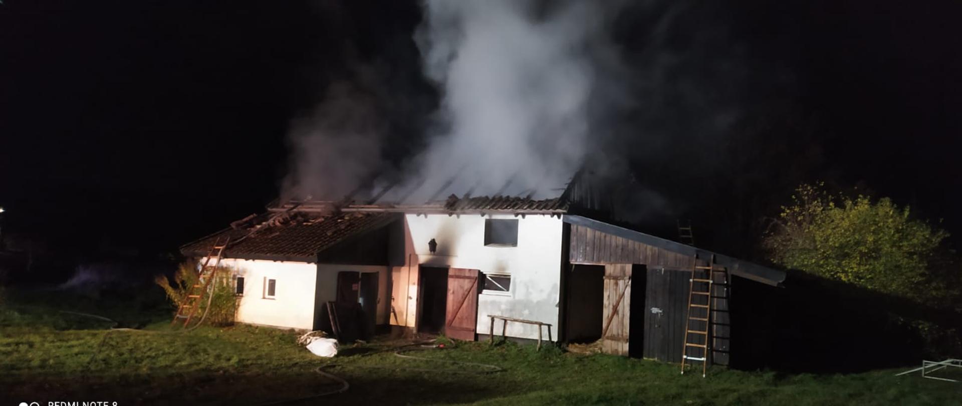 Pora nocna, na zdjęciu widać stojący budynek obory z którego wnętrza unosi się dym. Dach budynku doszczętnie spalony, widoczny tylko stelaż.