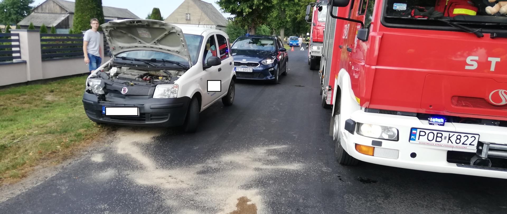 na pierwszym planie samochód strażacki z boku rozbity samochód osobowy 