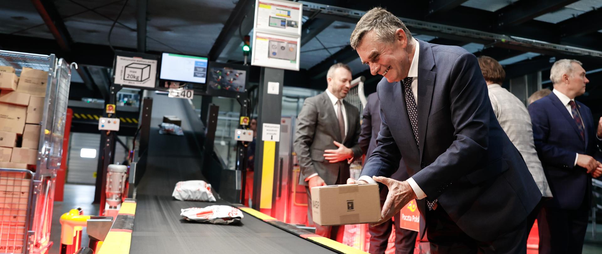 Wojewoda lubelski Lech Sprawka kładzie paczkę na taśmie produkcyjnej w sortowni Poczty Polskiej.