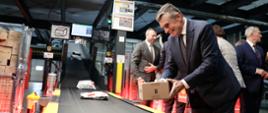 Wojewoda lubelski Lech Sprawka kładzie paczkę na taśmie produkcyjnej w sortowni Poczty Polskiej.