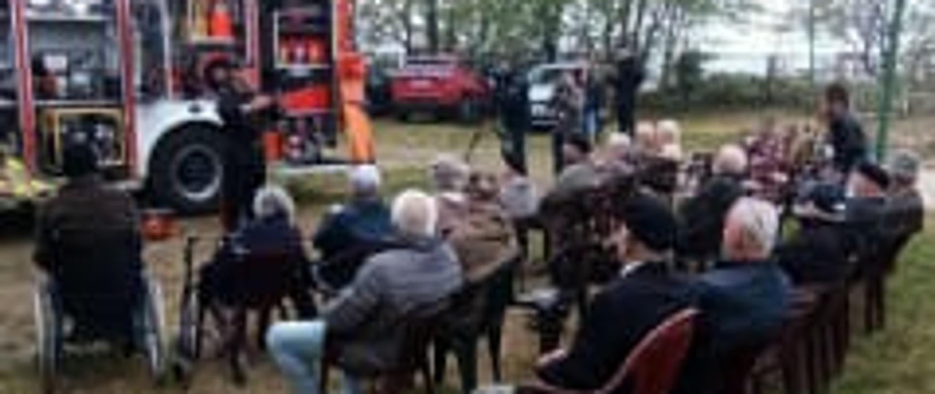 Grupa ludzi na świeżym powietrzu słucha wykładów na temat bezpieczeństwa.