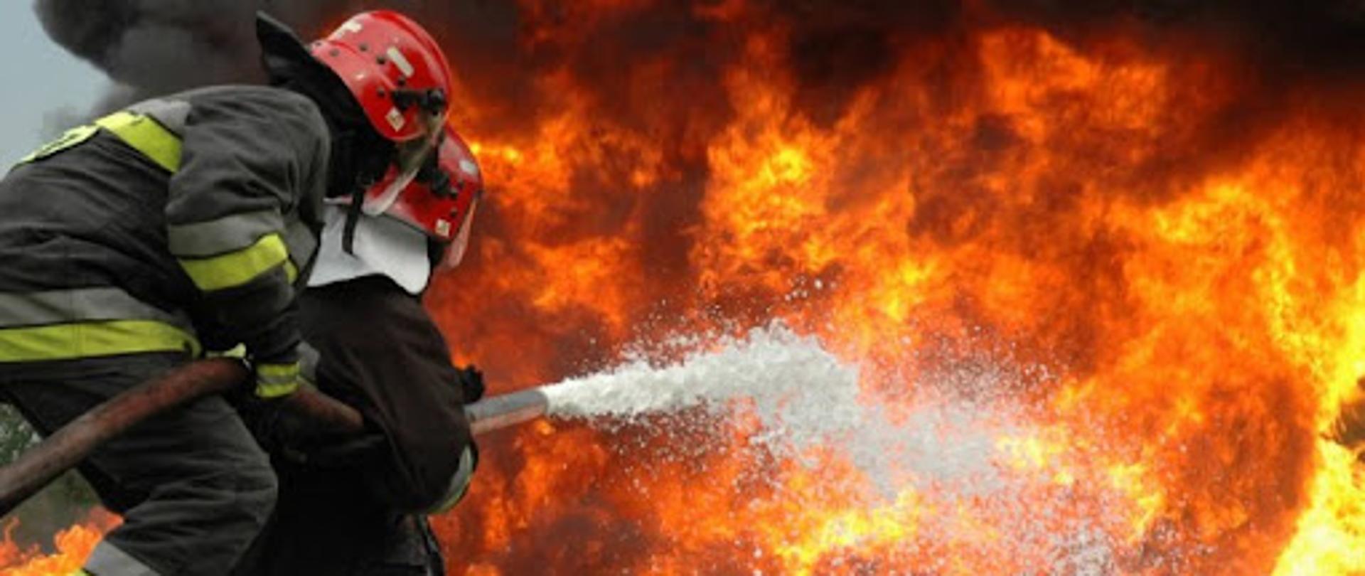 Strażacy gaszą płomienie piana gaśniczą.