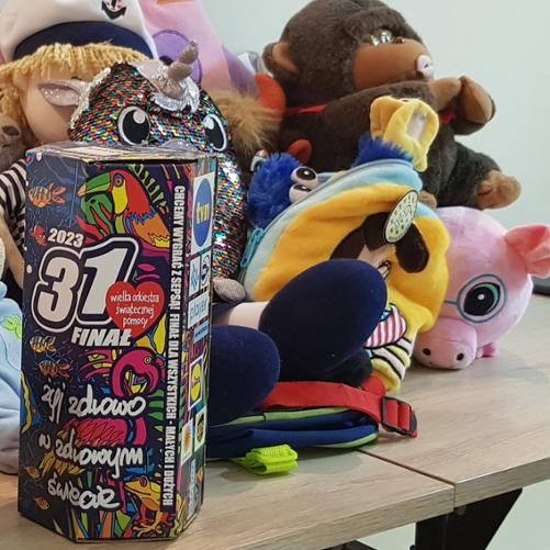 zdjęcie przedstawia pluszaki i fanty przeznaczone na licytację oraz puszkę z logiem Wielkiej Orkiestry Świątecznej Pomocy. 