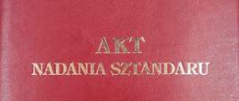 Na zdjęciu widzimy ozdobną okładkę do aktu nadania sztandaru. Okładka koloru czerwonego, na środku okładki na czerwonym tle złoty napis :"AKT NADANIA SZTANDARU". 