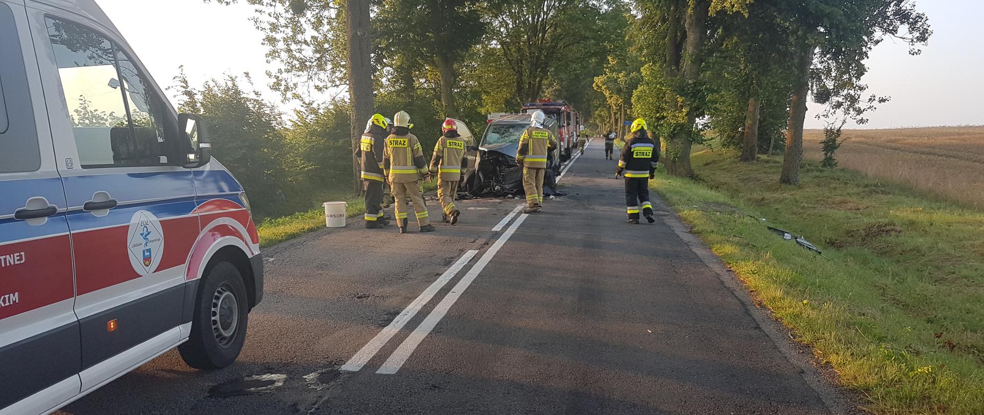 Zdjęcie przedstawia wrak pojazdu dostawczego VW oraz strażaków podczas końcowej fazy działań, gdzie prowadzona jest sorbcja płynów eksploatacyjnych