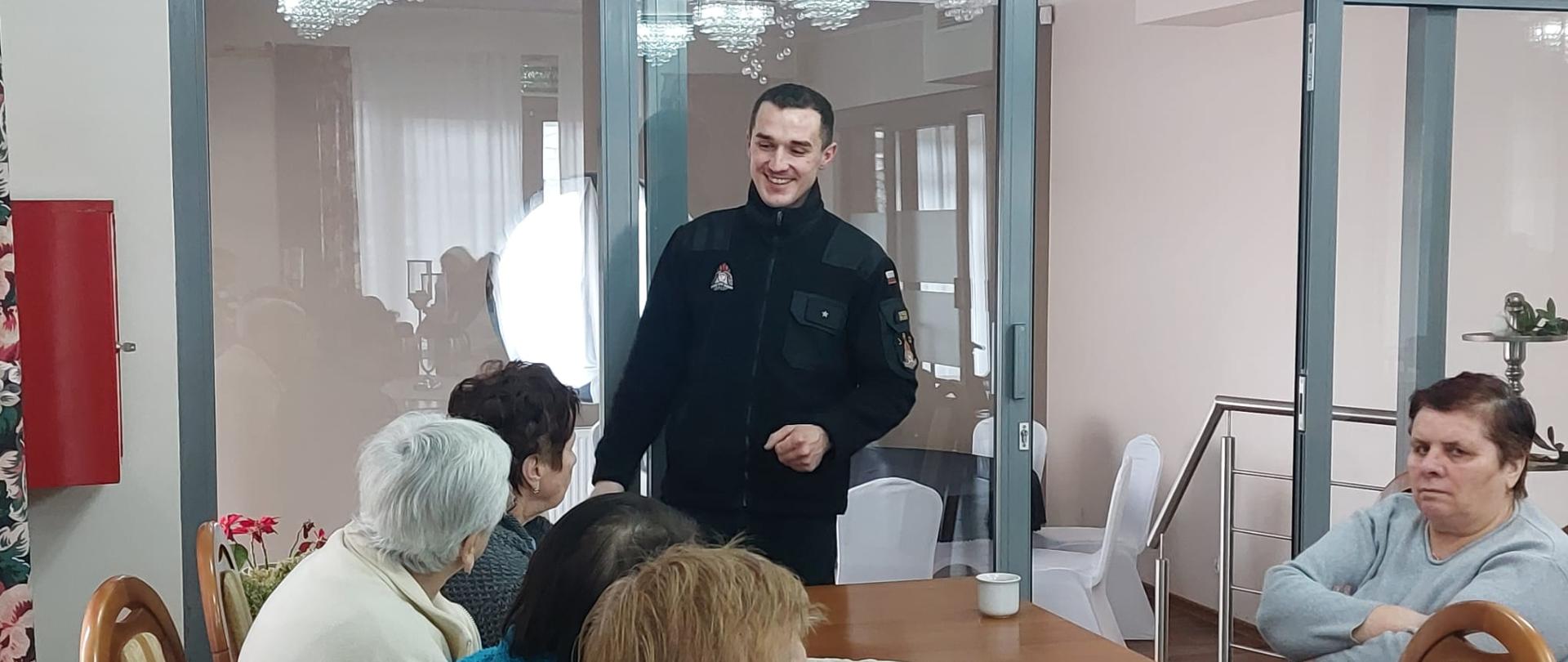 Na zdjęciu znajduje się strażak demonstrujący gaśnicę oraz kilka starszych osób