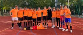 zdjęcie przedstawia drużynę w pomarańczowych koszulkach podczas wspólnego pozowanego zdjęcia po meczu, jeden z zawodników leży na boisku