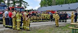 Zdjęcie przedstawia zbiórkę po ćwiczeniach na lasach. Strażacy stoją ustawieni w litere U i słuchaja podsumowania.