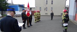 Zdjęcie wykonano porą dzienną, na placu Komendy Powiatowej Państwowej Straży Pożarnej w Sępólnie Krajeńskim. Przedstawia ślubowanie strażaka Radosława Rybarczyka (po prawej ) podczas uroczystego zdania i przejęcia zmiany służbowej. Starszy brygadier Maciej Suchomski ubrany w mundur wyjściowy wygłasza mowę, na dalszym planie poczet sztandarowy oraz strażacy ubrani w ubrania specjalne ustawieni w szeregu, a także dowódca zmiany ubrany w mundur służbowy stoją na baczność. 