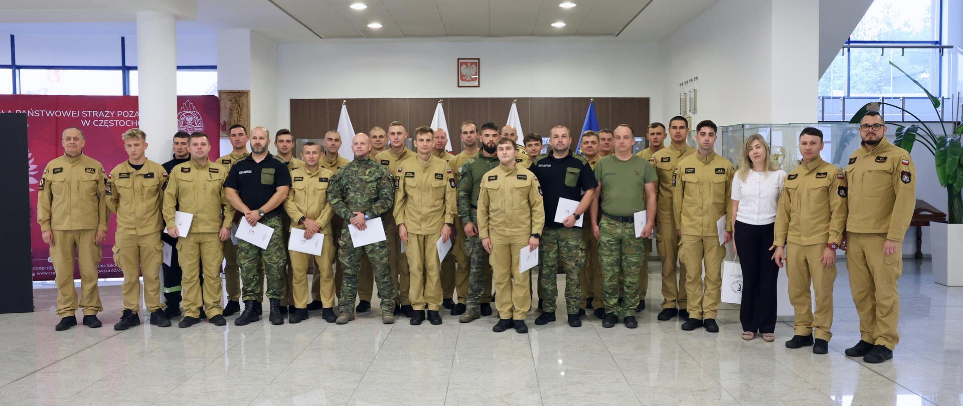 Pamiątkowe zdjęcie grupowe funkcjonariuszy PSP oraz Straży Granicznej będących uczestnikami szkolenia w zakresie przeciwdziałania zagrożeniom CBRNE (25 osób) w towarzystwie trzech funkcjonariuszy CS PSP oraz kobiety