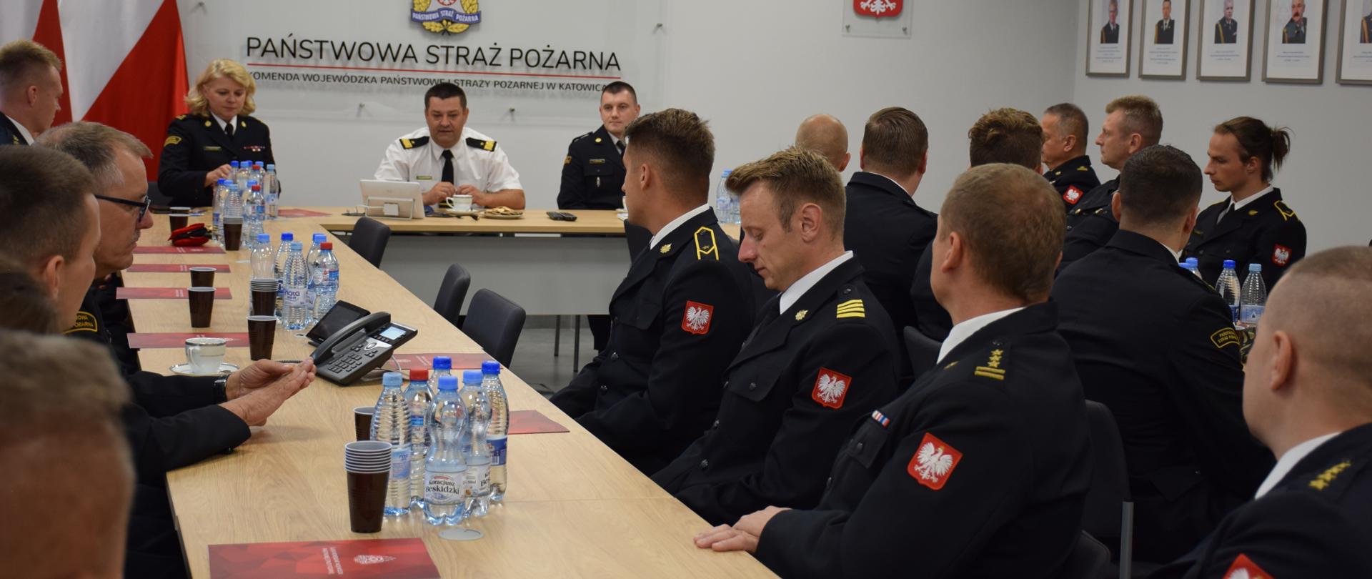 W sali sztabowej Komendy Wojewódzkiej PSP w Katowicach przy stole siedzą strażacy sportowcy, u szczytu stołu siedzi Śląski Komendant Wojewódzki PSP nadbryg. Jacek Kleszczewski z dwoma funkcjonariuszami 