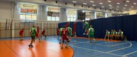 Zdjęcie przedstawia strażaków grających w piłkę siatkową na hali sportowej. 