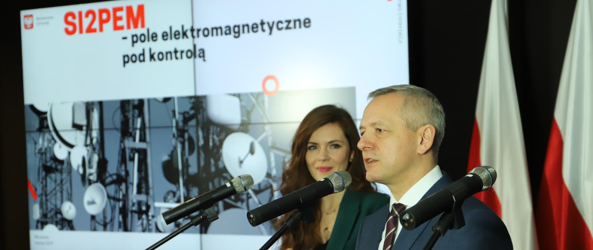 Minister Marek Zagórski i minister Wanda Buk na konferencji prasowej. W tle ekran z napisem "SI2PEM - pole elektromagnetyczne pod kontrolą".
