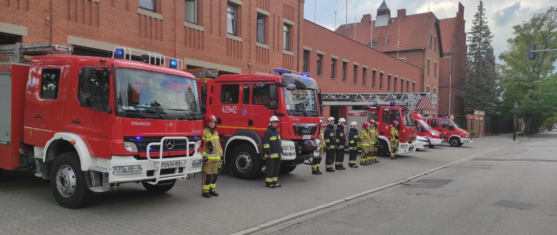 Strażacy obok wozów pożarniczych przed strażnicą KP PSP Gniezno stojący podczas uroczystej zbiorki z okazji 78 rocznicy Powstania Warszawskiego