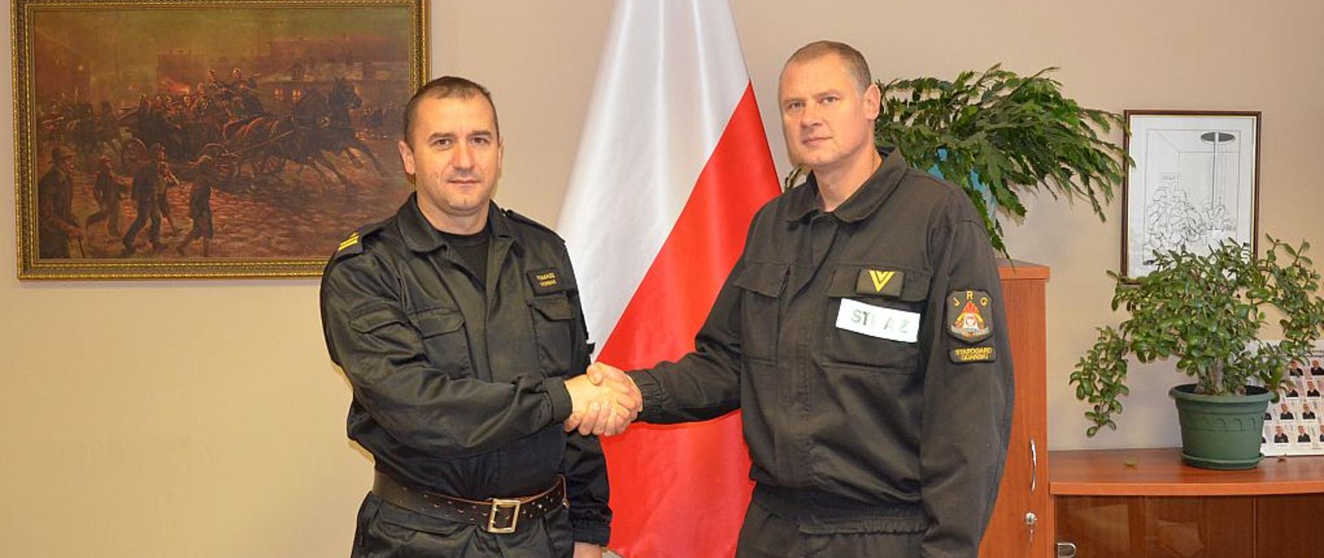 Zdjęcie przedstawia moment gratulacji składanych przez zastępcę komendanta, w tle flaga