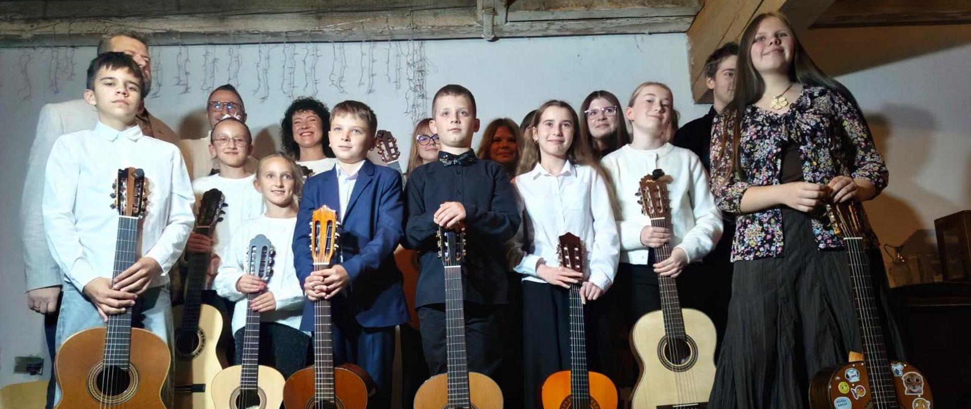 Galeria 10 zdjęć z występu uczniów klasy gitary w Pracowni Ceramiczno-Rzeźbiarskiej „Stary Młyn” w Gorzanowie. Młodzi gitarzyści prezentują swoje umiejętności muzyczne, wykonują przygotowane utwory i dzielą się pasją do muzyki, zdobywając cenne doświadczenie sceniczne w wyjątkowej przestrzeni artystycznej.