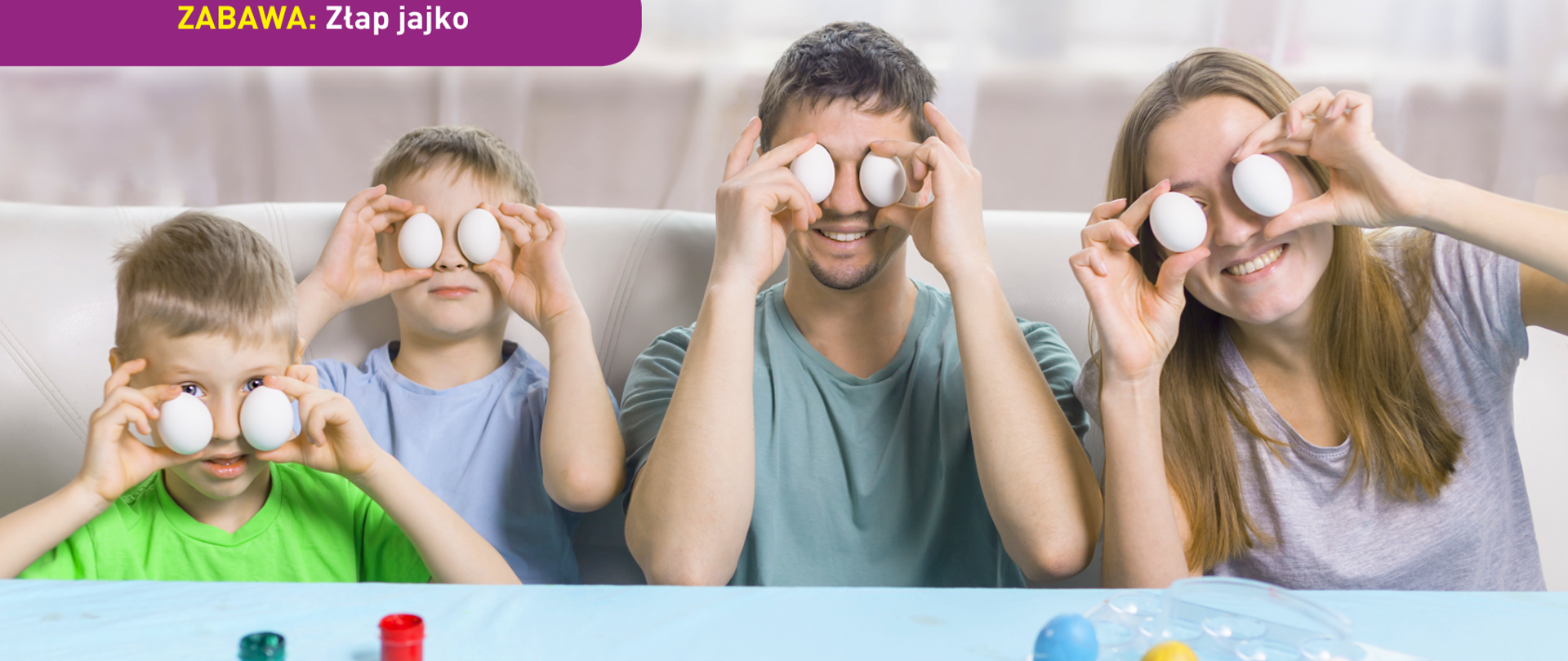 Zdjęcie przedstawia mężczyznę, kobietę i dwóch chłopców, wszyscy trzymają po jednym kurzym jajku w każdej dłoni w taki sposób, że jajka przesłaniają im oczy. Przed nimi na stole widać więcej jajek (pomalowanych) oraz farby. U dołu znajduje się pasek logotypów: Europejskie Fundusze Polska Cyfrowa, Ministerstwo Cyfryzacji, NASK i Unia Europejska Europejski Fundusz Rozwoju Regionalnego.