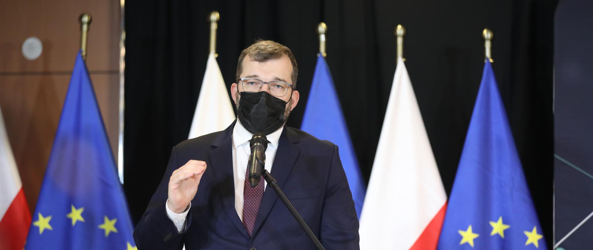 Minister Grzegorz Puda przemawia podczas konferencji w tle flagi Polski i Unii Europejskiej