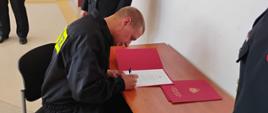 Zdjęcie przedstawia jednego z nowo przyjętych do służby podczas podpisywania, aktu ślubowania.