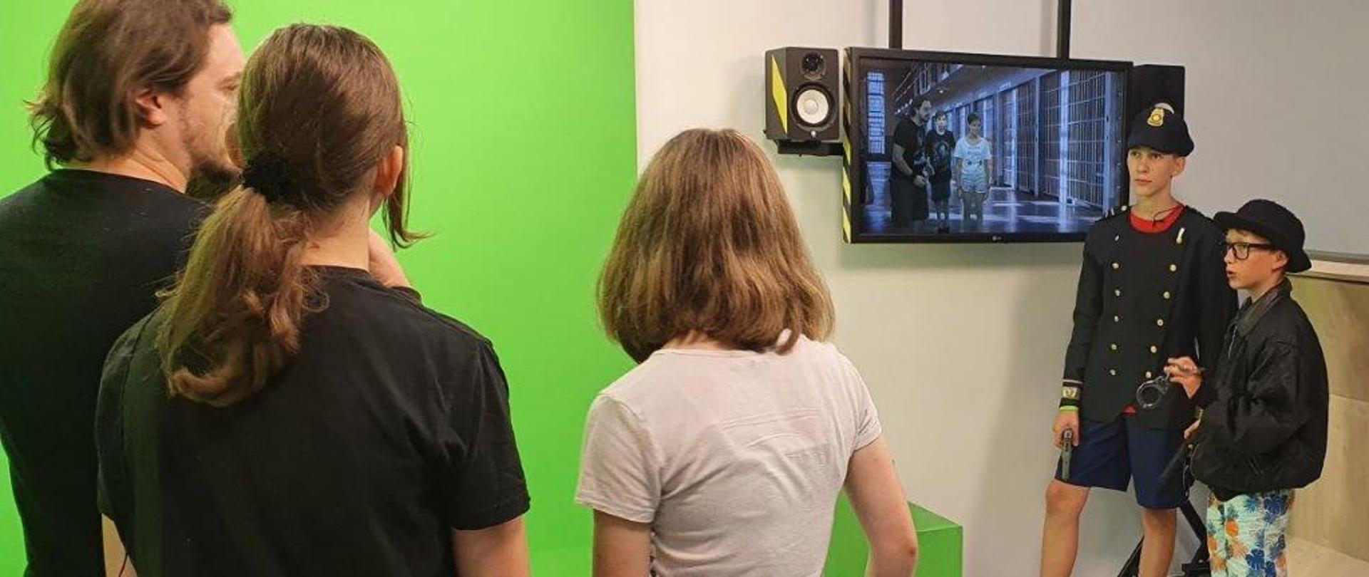 Dzieci w studio z zieloną ścianą oglądają na monitorze swoje nagranie 