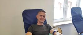 Na zajęciu widoczny mężczyzna siedzący na fotelu na sali oddający krew podczas akcji zbiórki krwi zorganizowanej przez Klub Honorowych Dawców Krwi Polskiego Czerwonego Krzyża przy Komendzie Powiatowej Państwowej Straży Pożarnej w Gorlicach i Klub Honorowych Dawców Krwi Polskiego Czerwonego Krzyża Moszczenica.