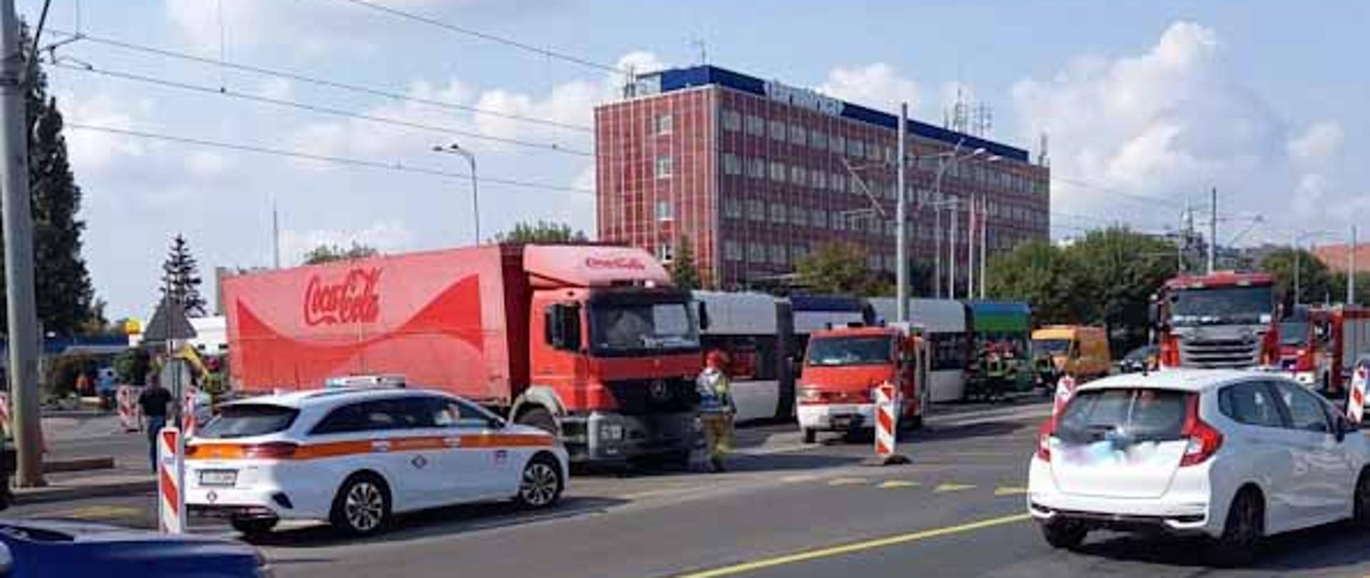  miejsce wypadku z oddali widać ciężarówkę oraz wozy straży pożarnej a w tle budynek biurowy