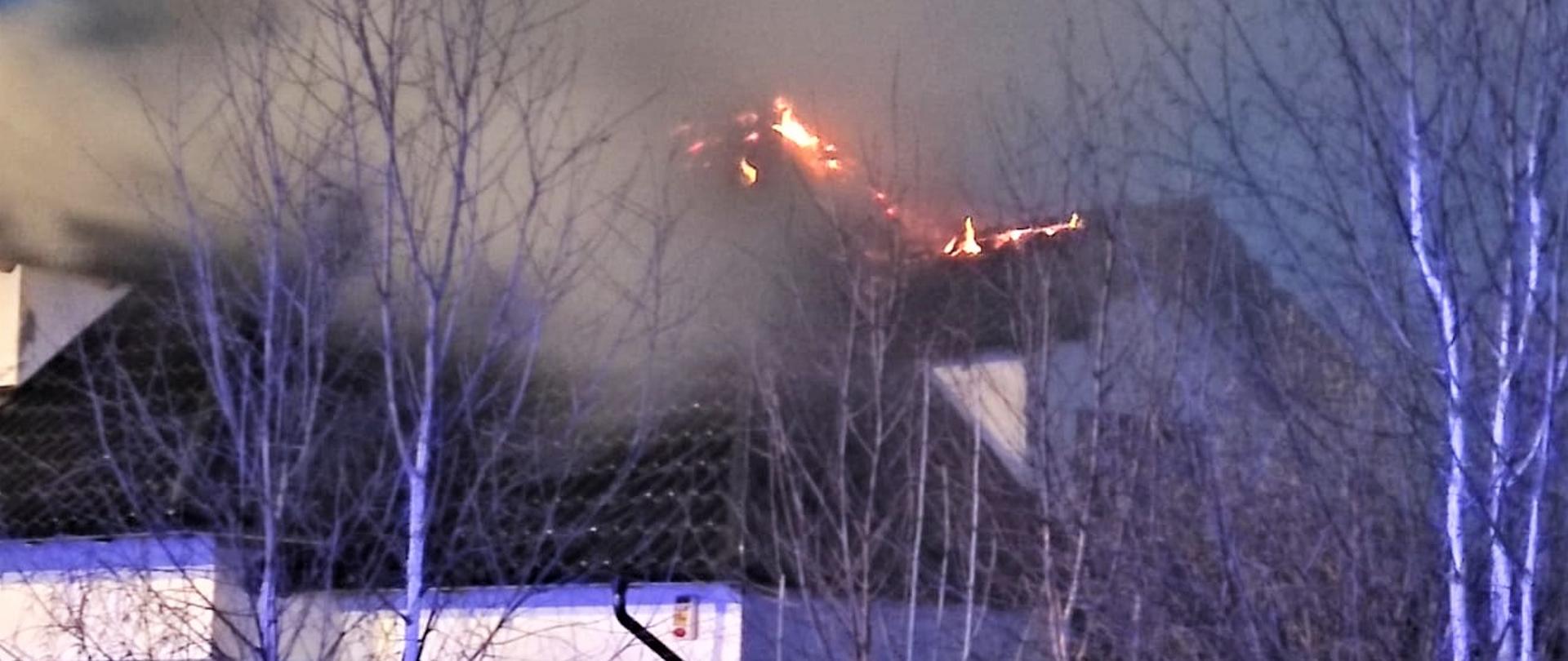 Na zdjęciu przedstawiono jednorodzinny budynek mieszkalny. Na dachu pokrytym dachówką ceramiczną widać płomienie.