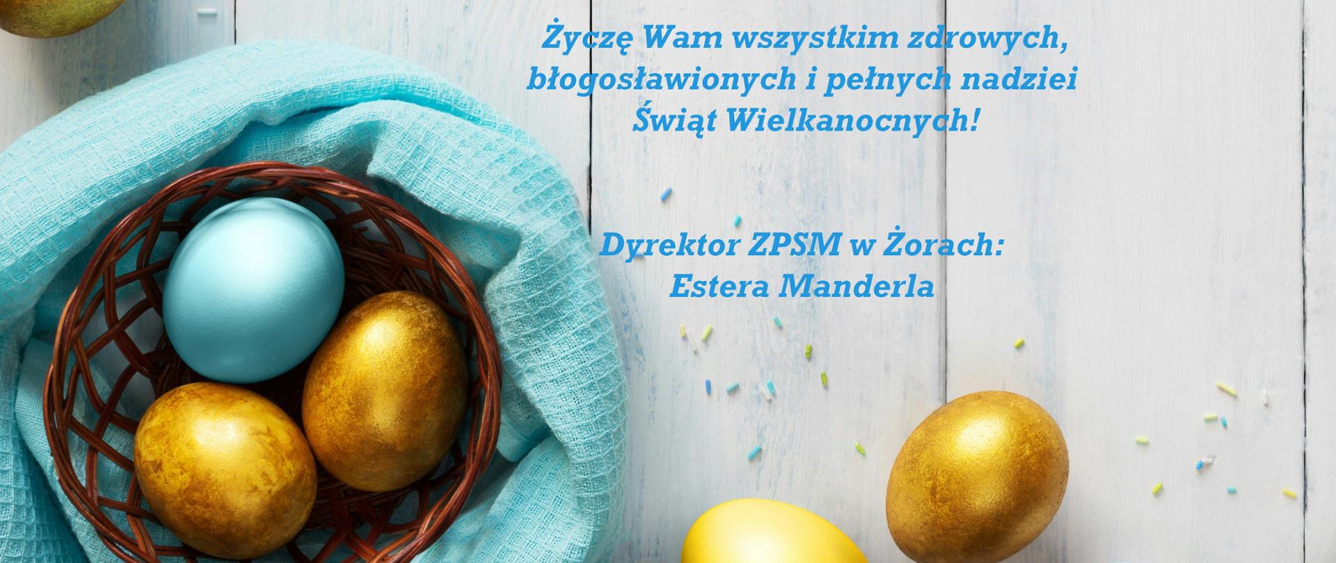 Kartka wielkanocna na jasnym, drewnianym tle. Po lewej stronie widoczne są kolorowe pisanki: złote i pastelowo-niebieskie, część z nich leży w małym, brązowym koszyku wyłożonym jasnoniebieską tkaniną. Wokół rozsypane są drobne, kolorowe dekoracje. Na środku znajduje się tekst życzeń wielkanocnych w języku polskim, zapisany niebieską czcionką. Życzenia skierowane są do nauczycieli, pracowników szkoły, uczniów i rodziców, podpisane przez dyrektora ZPSM w Żorach, Esterę Manderlę.
