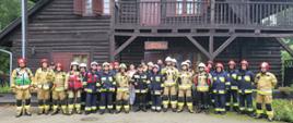 Pamiątkowe zdjęcie grupowe strażaków biorących udział w ćwiczeniach "WYSPA W OGNIU" W tle zabytkowy drewniany Domek Szwajcarski na Wyspie Edwarda w Zaniemyślu