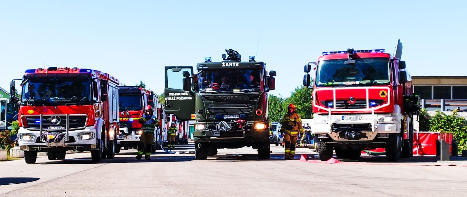 Zdjęcie przedstawia pojazdy pożarnicze oraz strażaków przygotowujących się do akcji gaszenia pożaru lasu podczas ćwiczeń powiatowych „Gucin 2023”